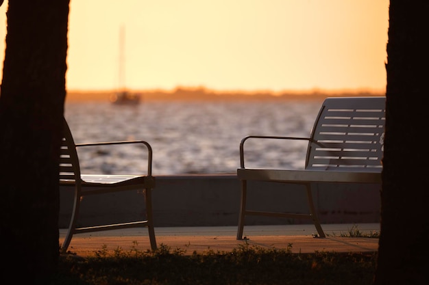 Resting bench in public park on sea shore at sunset