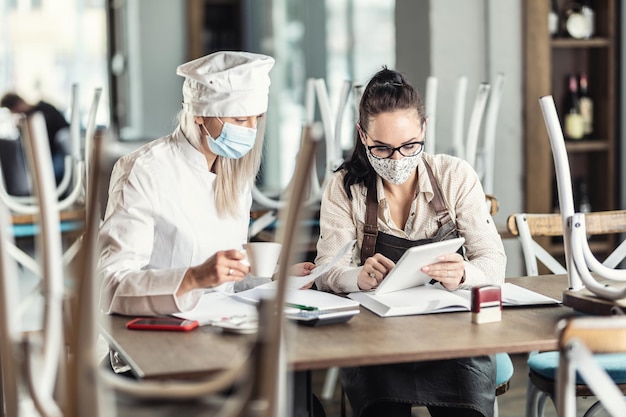 Restuarant chef and waitress calculate finances over coffee sitting in a closed bar