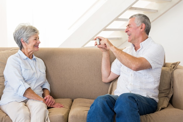 Retired man taking photo of his partner on the couch