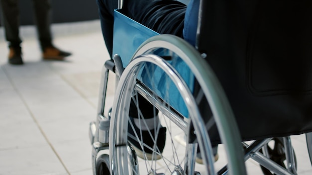 Retired person with physical impairment waiting in reception lobby to start checkup visit appointment with medic. Wheelchair user with disability in waiting room area at facility. Close up.