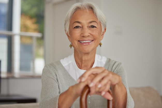 Retired senior woman relaxing at home Happy smiling old woman holding walking cane and looking at the camera with positivity Carefree and mature grandmother sitting on chair in nursing home