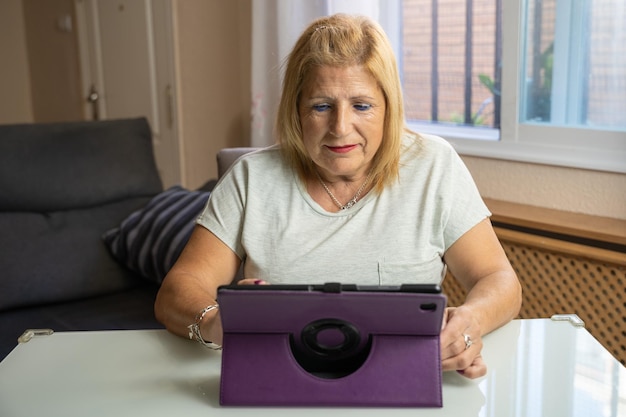 Retired woman sitting with her tablet while watching playing or talking to someone and being entertained and content