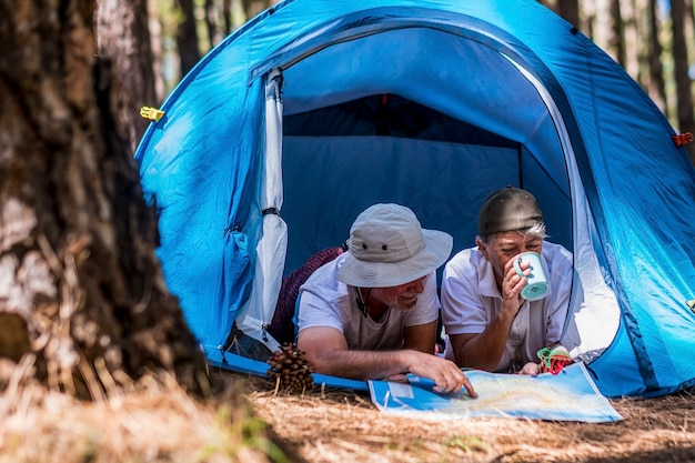 Retirement couple lifestyle enjoy travel tourism vacation laying inside a tent in free wild camping outdoor - aged people and feeling with nature woods forest experience - elderly traveler