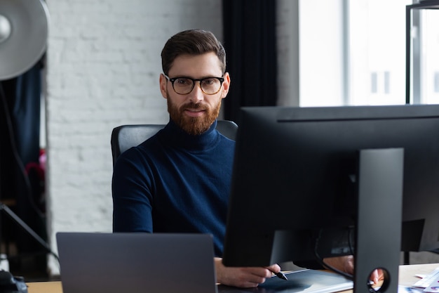 Retouching images in special program.Portrait of graphic designer working in office with laptop,monitor,graphic drawing tablet and color palette.Retoucher workplace in photo studio.Creative agency.