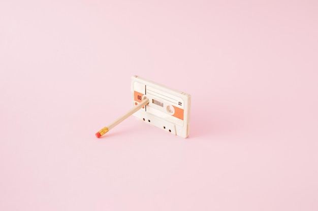 Retro audio cassete with lead pencil stucked in a reel on pink background