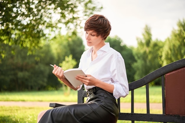 Retro image of a stylish beautiful woman sitting in a park on a bench with a book in her hands The concept of style and fashion