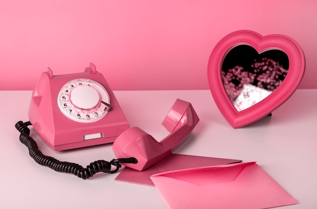 Retro phone with heart mirror and envelopes at table still life in pink color valentines day concept...