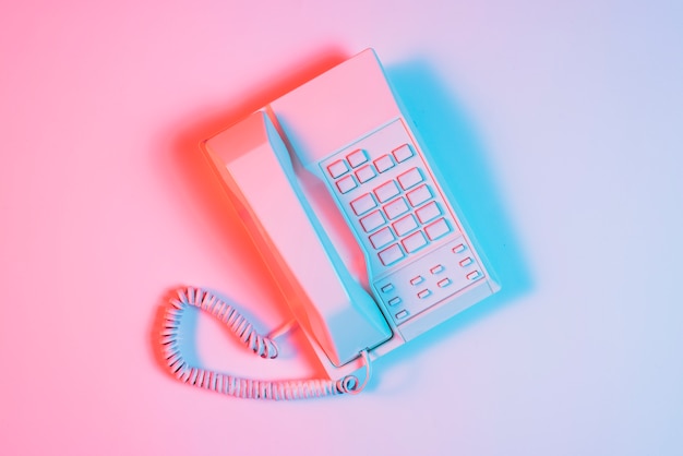 Retro pink telephone with blue light on pink surface