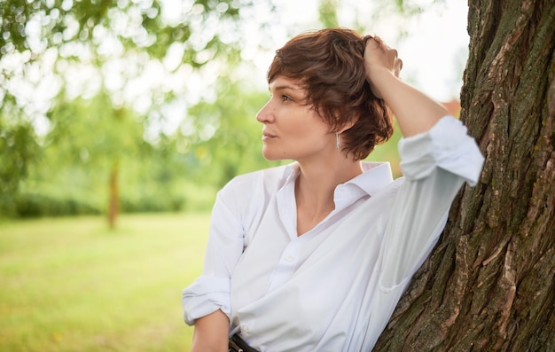 Retro portrait of a stylish beautiful woman in a white shirt on the background of a sunny meadow The concept of style and fashion