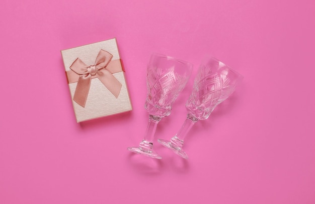 Retro style faceted crystal wine glasses and gift box on pink background Christmas concept Top view