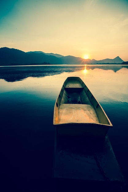 retro sunset over lake and mountain with small wooden fisherman boat