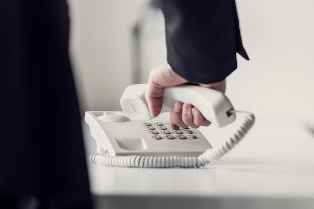 Retro toned image of a businessman dialing telephone number on a classical white landline telephone, low angle view between his arm and body.