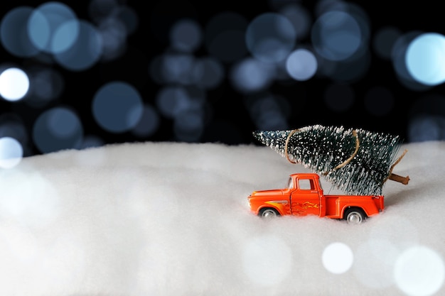 Retro toy car with a Christmas tree in snowdrifts, and blurred lights. Christmas background. Holiday postcard