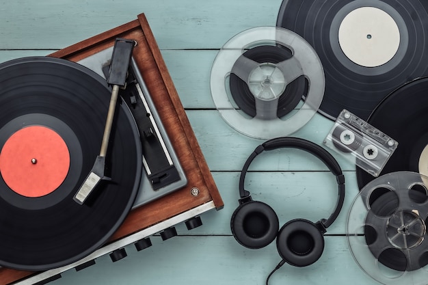 Retro vinyl record player with records, audio magnetic reel, audio cassette and stereo headphones on blue wooden background. Top view. Flat lay