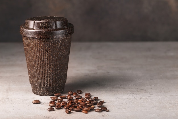 Reusable brown coffee cup with coffee beans on grey background and brown wall