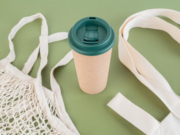 Photo reusable cup on green background surrounded by reusable cloth bags environment and sustainability