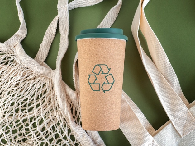 Photo reusable cup with recycling icon on reusable cloth bags and green background sustainability recycling and environment