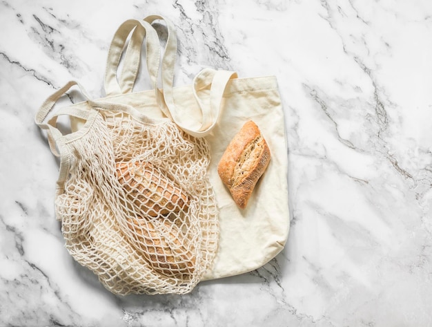 Reusable eco bags and buns on a light marble background top view