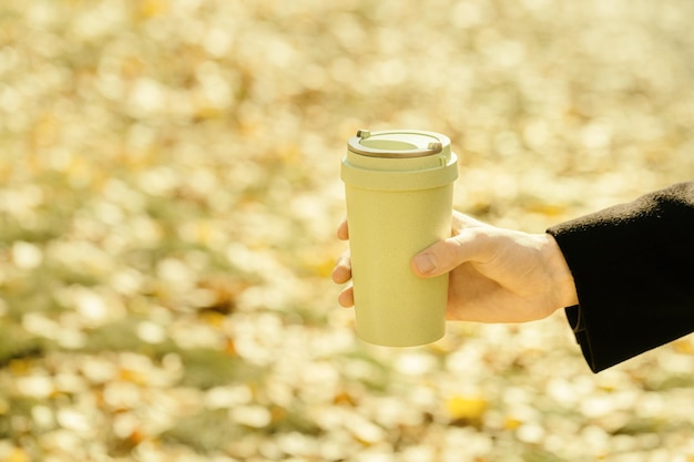 Reusable eco friendly bamboo cup with lid for take away coffee close up in hands on autumn