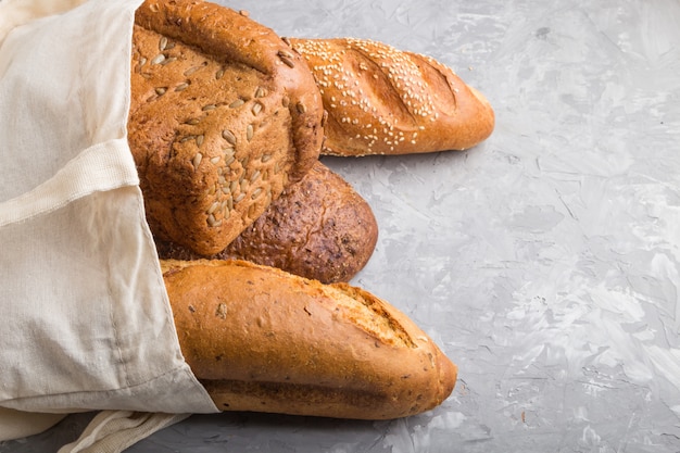 Reusable grocery bag with fresh baked bread on a gray concrete background. side view, copy space.