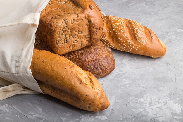 Reusable grocery bag with fresh baked bread on a gray concrete background. side view, copy space.