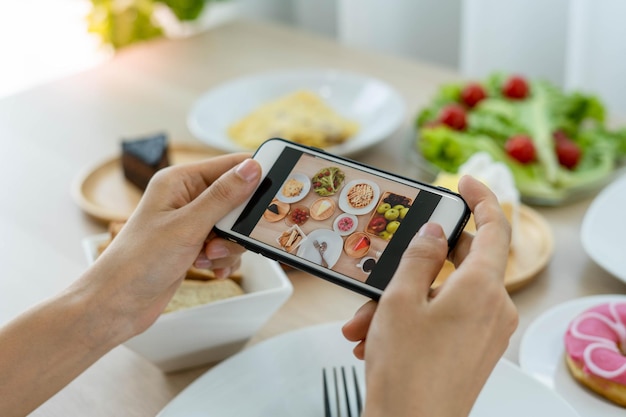 A reviewer's hand using a mobile phone to take pictures of food at a restaurant tableTake photo to write a review of the restaurant to share on the internet