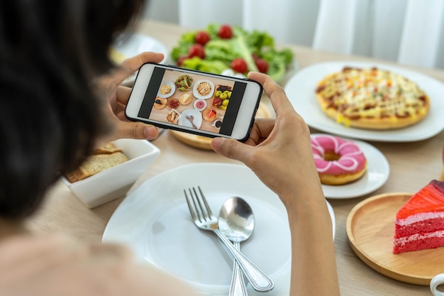 A reviewer's hand using a mobile phone to take pictures of food at a restaurant tableTake photo to write a review of the restaurant to share on the internet