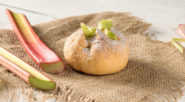 Rhubarb bun and rhubarb stalks on a burlap napkin on a wooden table