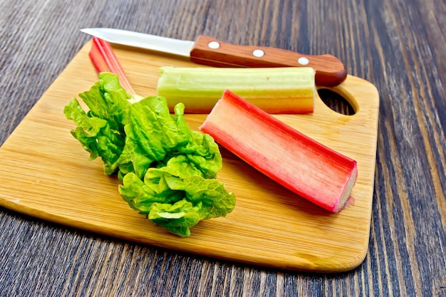 Rhubarb with knife and leaf on dark board