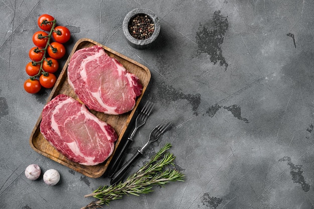 Rib eye steaks with spices set, on gray stone table background, top view flat lay, with copy space for text