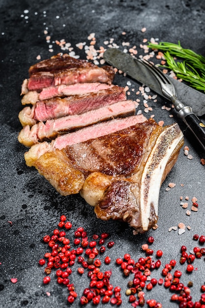 Ribeye steak on the bone with salt and pepper. Grilled Beef meat.  Black surface. Top view.