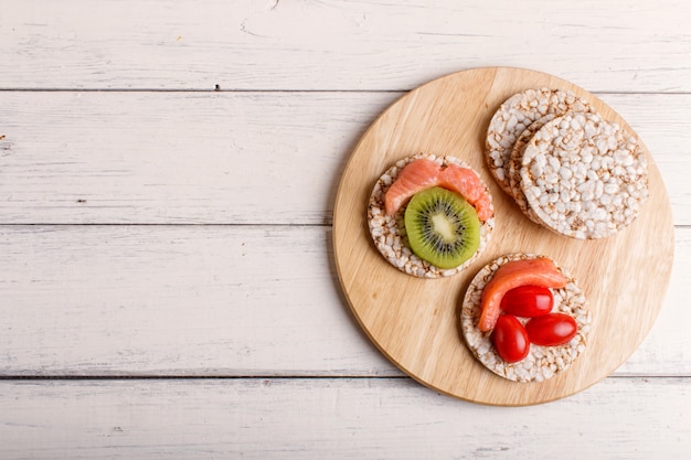 Rice cakes with salmon, kiwi and cherry tomatoes on white wood