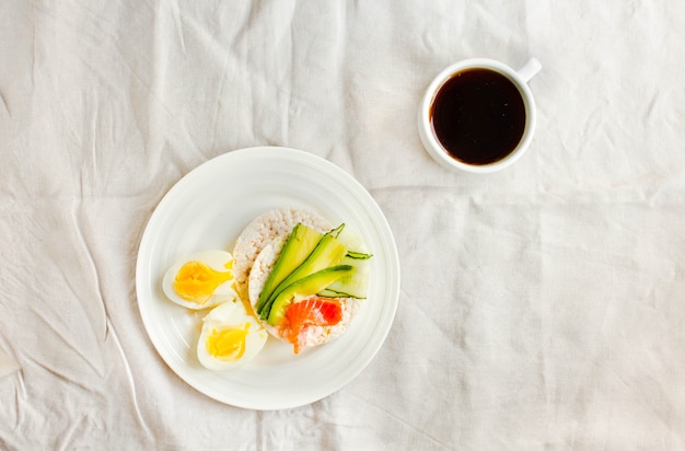 Rice crispy cakes with avocado and fresh salted salmon. Cup of coffee. Top view. Space for text. High protein and low carbohydrate meal. White linen tablecloth background.