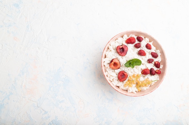 Rice flakes porridge with milk and strawberry in ceramic bowl on white concrete surface