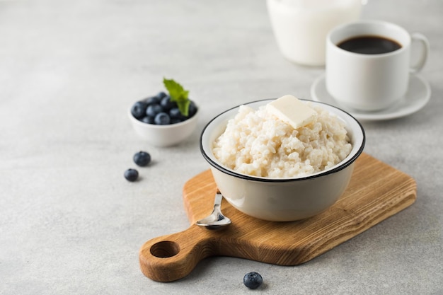 Rice porridge or pudding with a piece of butter a mug of coffee and blueberries in a bowl Copy space