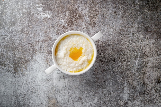 Rice porridge with butter in a white cup against a gray stone table. A healthy breakfast in a restaurant