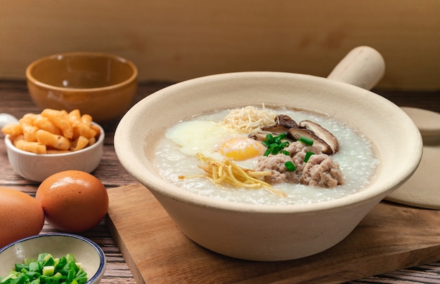 Rice porridge with soft boiled egg and minced egg in white clay pot side dish with crispy patongo deep fried dough stick  Thai breakfast