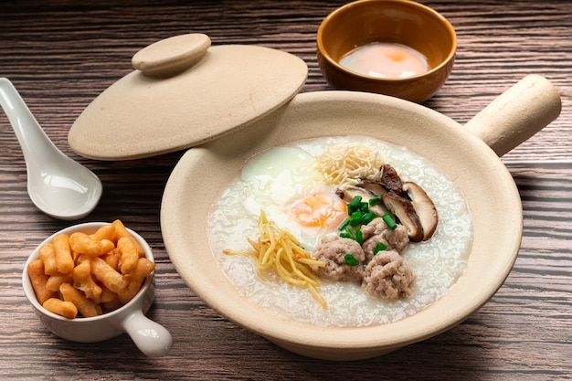 Rice porridge with soft boiled egg minced pork ball sliced shiitake mushroom sliced ginger in clay pot serving with topping Crispy Patongo deep fried dough known as thai famous breakfast