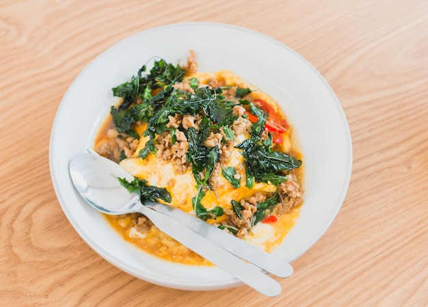 Rice topped with omelet with stir-fried pork and basil on wooden table