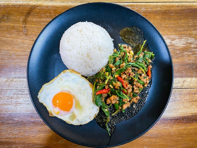 Rice topped with stirfried pork and basil with a fried egg on the table