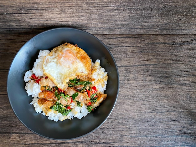 Rice topped with stirfried pork and basil with a fried egg on the table