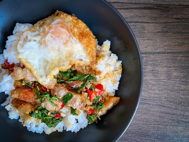 Rice topped with stirfried pork and basil with a fried egg on the table