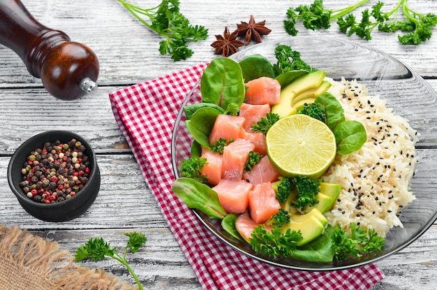 Rice with salmon avocado and spinach In a black plate on a wooden background Top view Free space for your text Flat lay