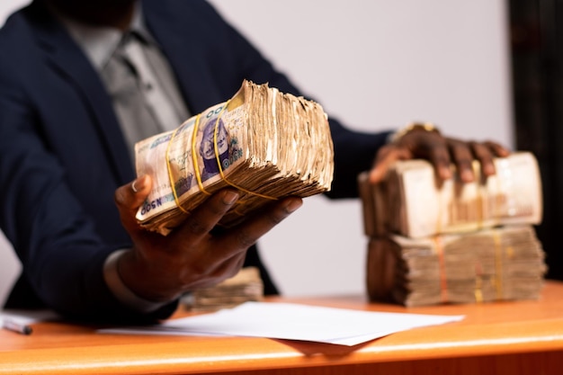 Photo rich african businessman sitting at his desk and holding huge bundles of cash