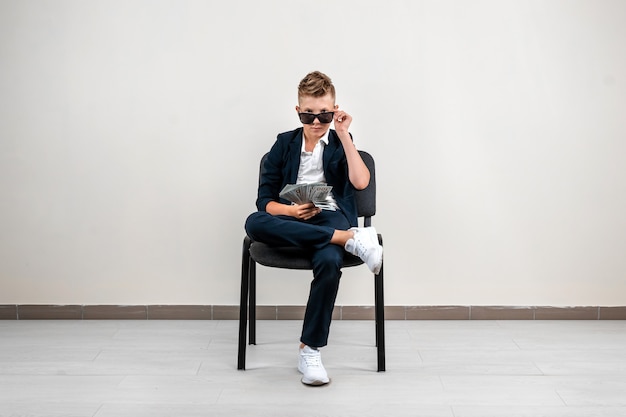 A rich boy on a light background holds a bundle of dollars in his hands. Financial education