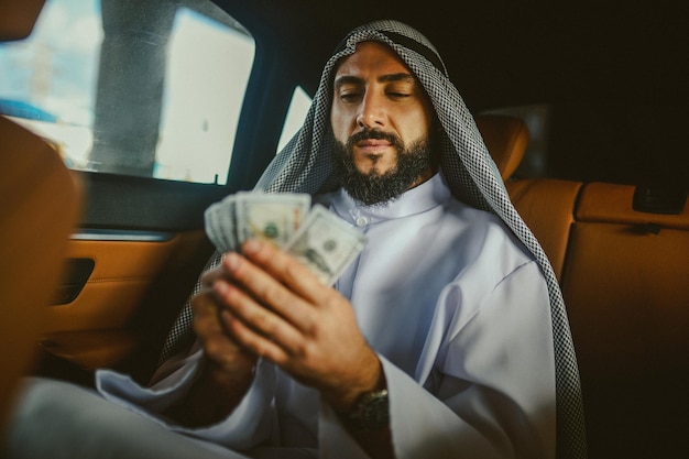 A rich man An arabian man in a traditional clothing in a car holding money