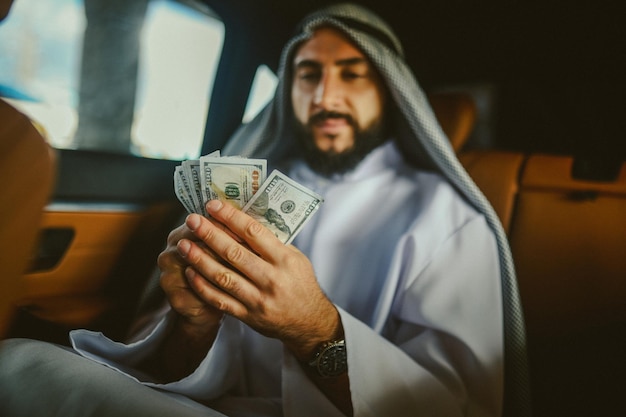 A rich man An arabian man in a traditional clothing in a car holding money