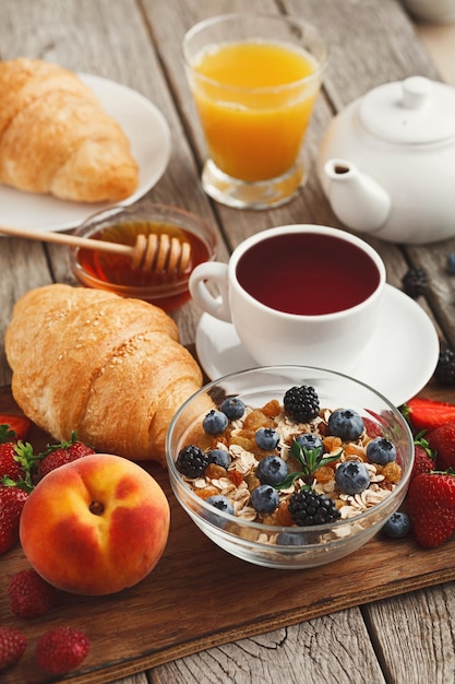 Rich tasty breakfast background. Croissants with golden crust, glass of fresh orange juice, lots of sweet organic berries and coffee on wooden board over rustic surface. Delicious start of the day