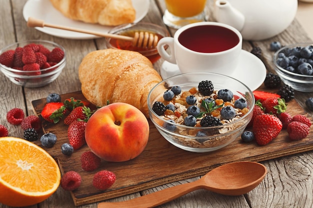 Rich tasty breakfast background. Croissants with golden crust, lots of sweet organic berries and coffee on wooden board over rustic surface. Delicious start of the day