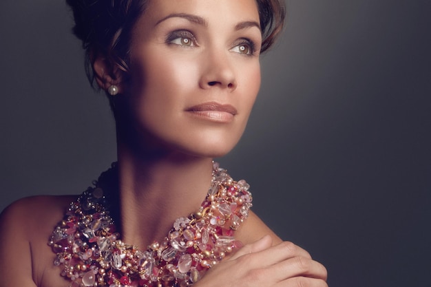 Rich woman elegant and necklace jewelry isolated on a dark background in a studio thinking of vintage beauty ideas and a mature female model with vision for classic cosmetics and makeup